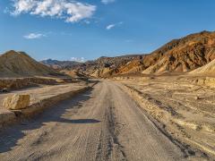 The leading line of Twenty Mule Team Canyon gravel road with golden badlands on either side, Death Valley National Park