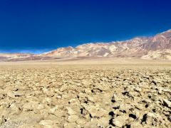 A dry, wrinkled, uneven surface with dry mountains in the background and clear blue sky overhead at Devil's Golf Course in Death Valley National Park