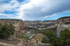 A river meandering between tall beige cliffs beneath a blue sky with dramatic clouds in Dinosaur National Monument