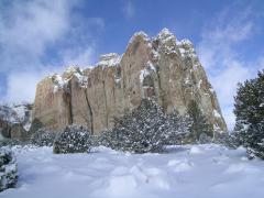 A thick blanket of snow covers the ground and several green trees, El Morro's rock face rises up in the background