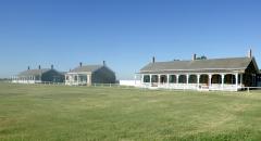 A long building facing a large green parade ground underneath a clear blue sky, Fort Larned National Historic Site