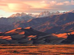 Orange light of sunset bathing Star Dune and the Crestone Peaks with fluffy yellow clouds overhead, Great Sand Dunes National Park and Preserve