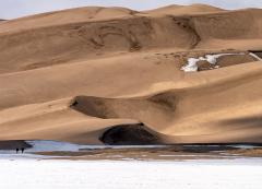 A telephoto view of the sinuous and shadowy sand dunes above a winter ground of snow and ice, Great Sand Dunes National Park and Preserve