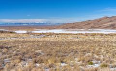 A wide expanse of scrub brush, snow-covered flat land, dunefield edge, San Luis Valley, and distant San Juan Mountains all beneath a clear blue sky, Great Sand Dunes National Park and Preserve