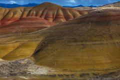 Afternoon sunlight and shadow over bright maroon-red and olive-yellow velvety hills at the Painted Hills Unit of John Day Fossil Beds National Monument