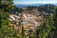 An overview of the steaming Bumpass Hell area framed by green pine trees, Lassen Volcanic National Park