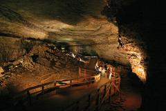 a large cave room lit up to show a boardwalk running through the middle of it with a group of people walking along it in Mammoth Cave National Park
