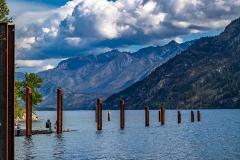 Two people sitting at the edge of the dock at the Stehekin Landing, viewing the downlake mountain scenery of Lake Chelan National Recreation Area.