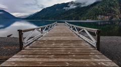A leading line created by the dock at Lake Crescent Lodge taking the viewer's eyes from the beach out over the clear water of Lake Crescent to view late summer mountain scenery in Olympic National Park