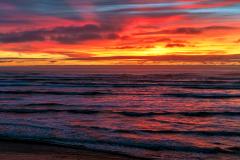 Layers of colorful clouds colored orange and gold by the setting sun over the Pacific Ocean and Kalaloch Beach, Olympic National Park