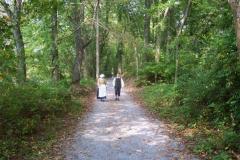 A man and woman in period costume walk along a wooded trail at Sycamore Shoals State Historic Area, Overmountain Victory National Historic Trail