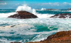 The teal-blue sea and waves crashing over large rocks at Pacific Rim National Park Reserve