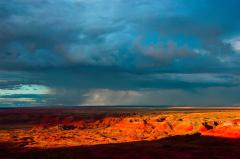 A sky darkened with monsoon rain clouds and a strip of sunlight saturating the landscape of Painted Desert at Petrified Forest National Park