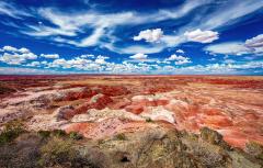 A view of the orange, red, and beige dunes of Painted Desert above a blue sky with puffy clouds at Petrified Forest National Park.