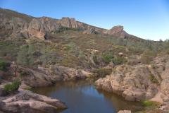 Bear Gulch Reservoir lined on either side by rock formations and scrub brush in Pinnacles National Park in California