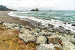 A hazy view of the teal-colored water of the Pacific Ocean and a rock and sand beach, with nearby sea stacks at Del Norte Redwoods State Park, Redwood National and State Parks