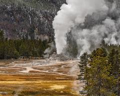 A person sits on a bench watching Castle Geyser erupt at Upper Geyser Basin at Yellowstone National Park