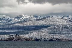 A telephoto view of snow-dusted mountains and trees across to the other side of the shoreline along Yellowstone Lake in Yellowstone National Park