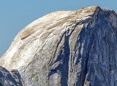 A telephoto close-up of a portion of Half Dome, with tiny ant-like people climbing the granite rock wall of the formation using installed cables in Yosemite National Park