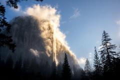 Morning clouds and fog streaming up El Capitan with the sun shining on the cliff face in Yosemite National Park in California